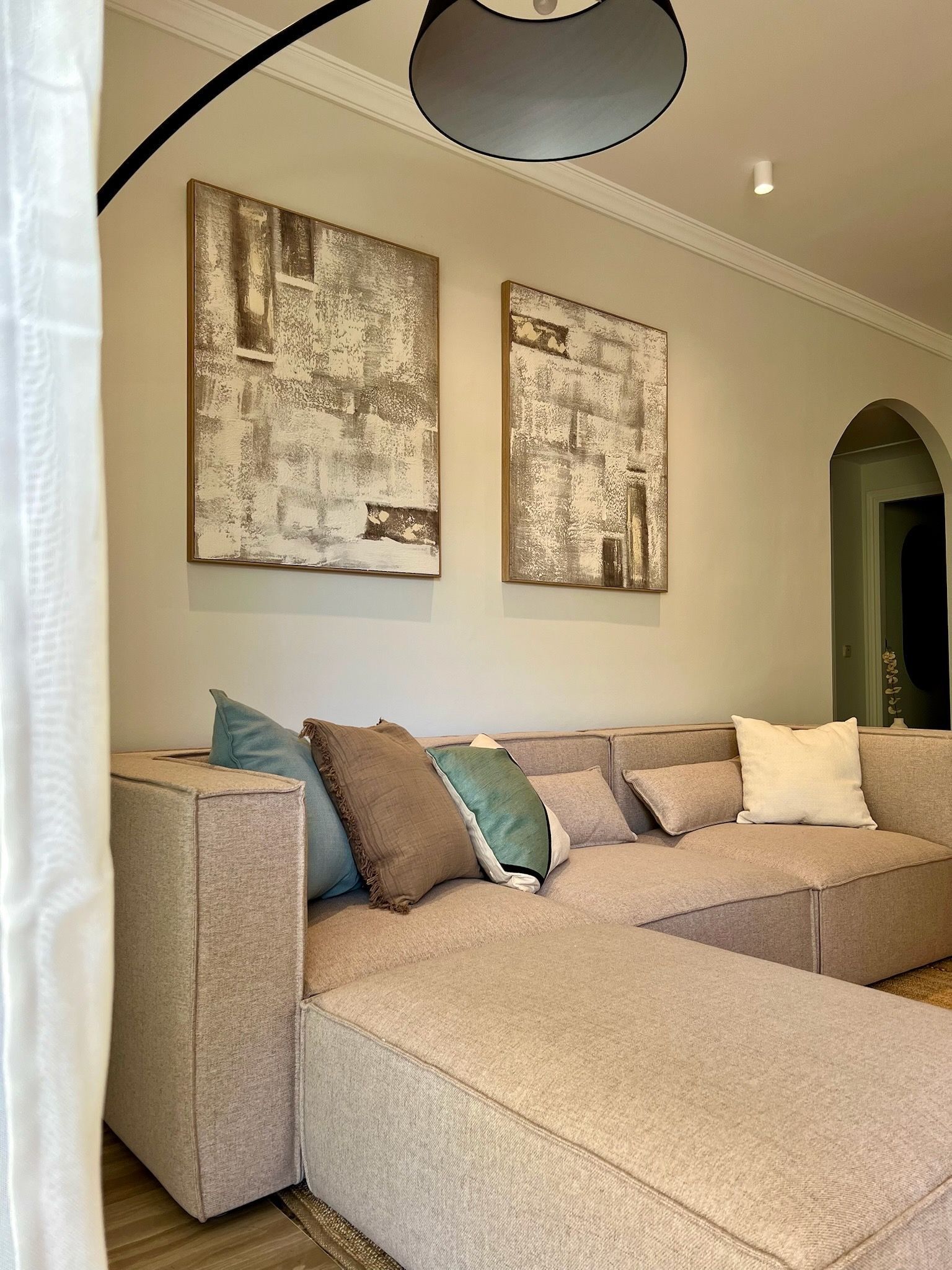 Sofá modular beige en una acogedora sala de estar con arte abstracto en la pared y una puerta arqueada.