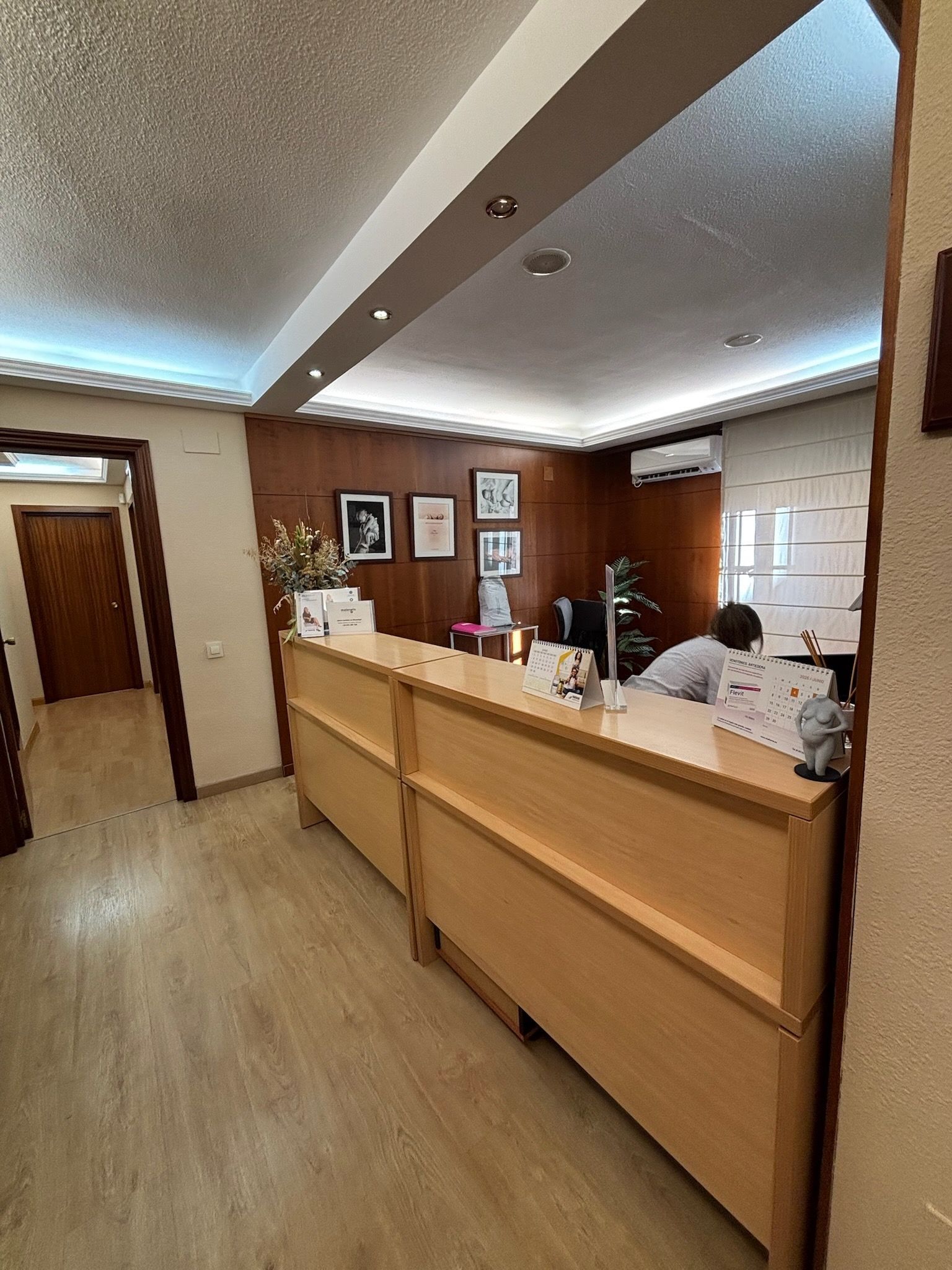Mostrador de recepción en el vestíbulo de una oficina moderna, con dos personas sentadas detrás y un cálido suelo de madera.