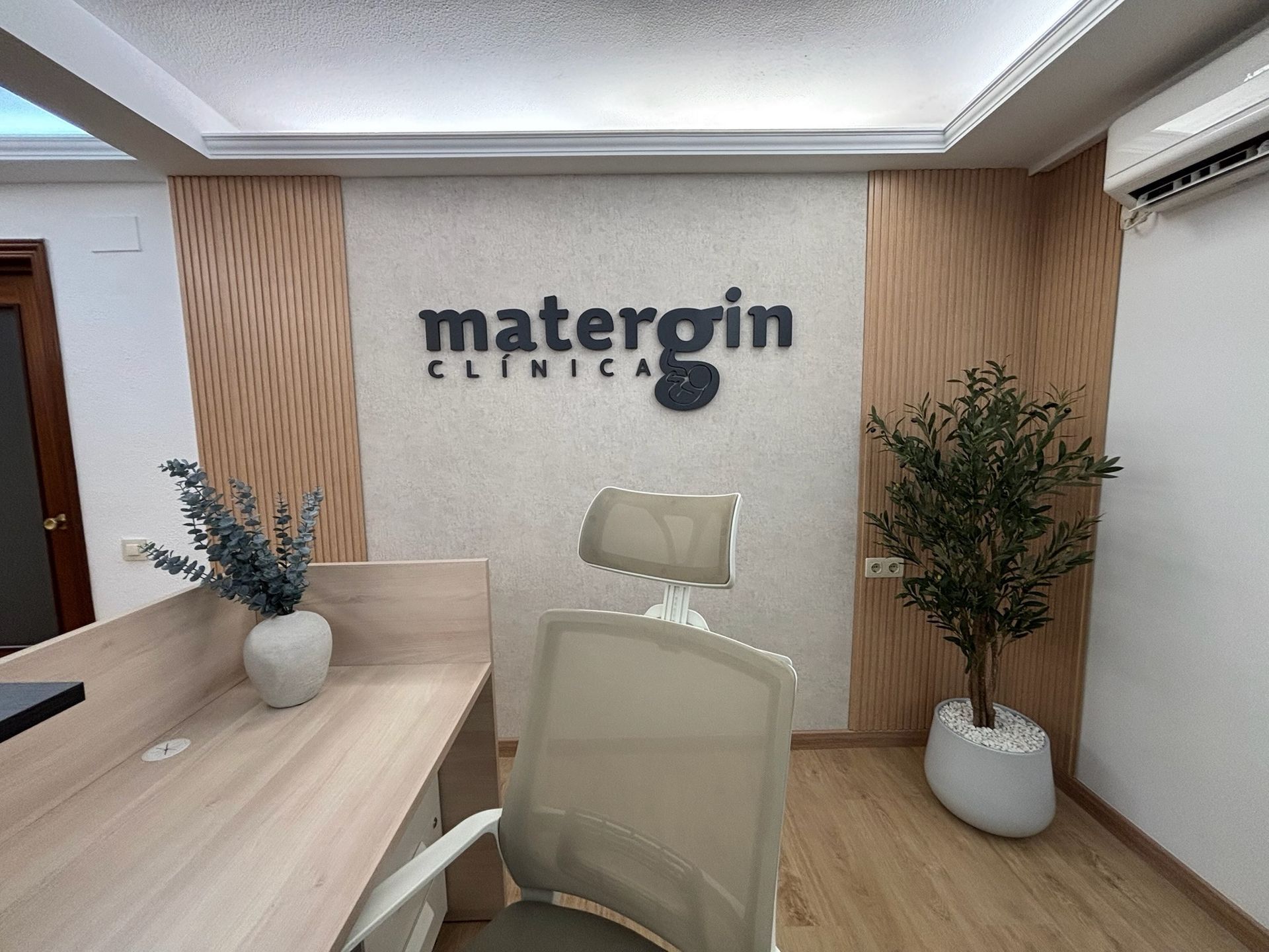Recepción de la clínica con sillas beige, escritorio, plantas y letrero de pared con la inscripción 