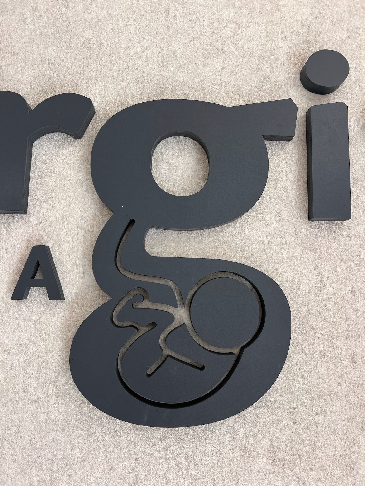 Letrero de pared negro y gris con letras estilizadas y un gran logotipo de la letra 
