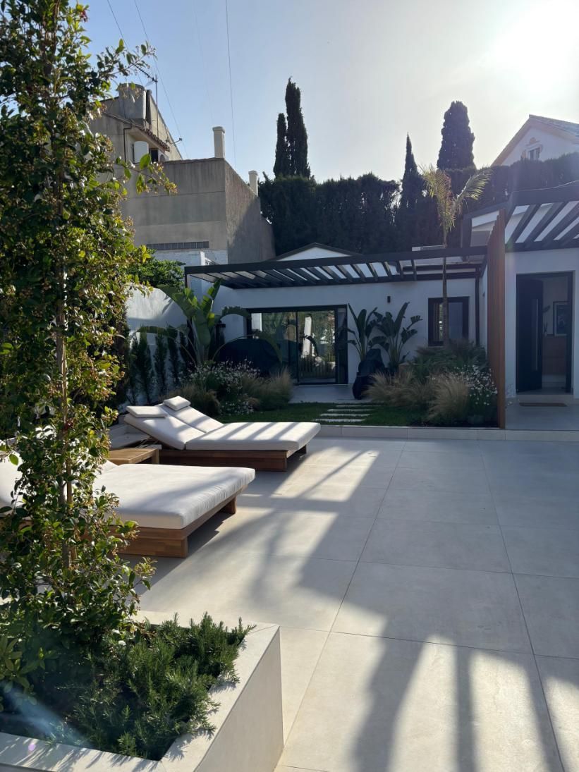 Patio soleado con tumbonas, plantas en macetas y una moderna fachada de casa en blanco y negro.