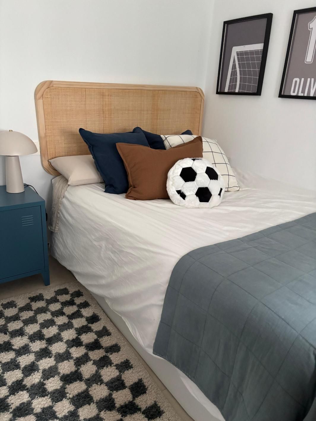 Cama bien hecha con cabecero tejido, ropa de cama azul grisácea y balón de fútbol en un dormitorio moderno.