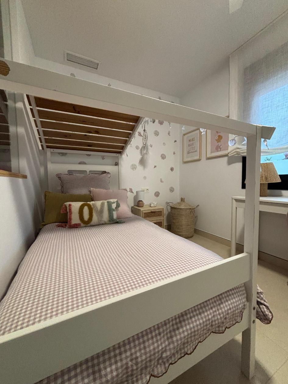 Litera blanca en una habitación con estampado floral, con una colcha de rayas rosas y una almohada con la palabra 