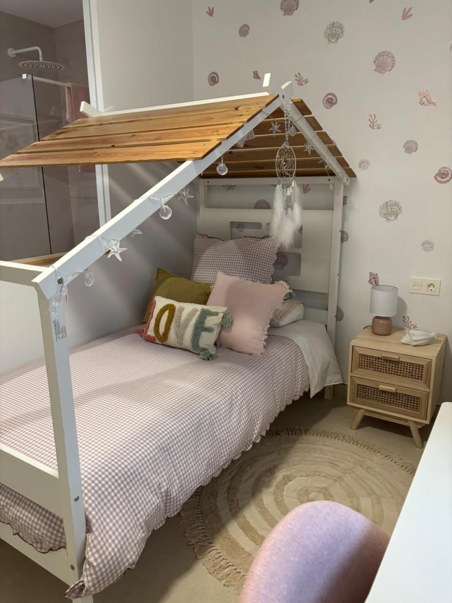 Cama infantil con forma de casa, con ropa de cama y almohadas rosas en una acogedora habitación.