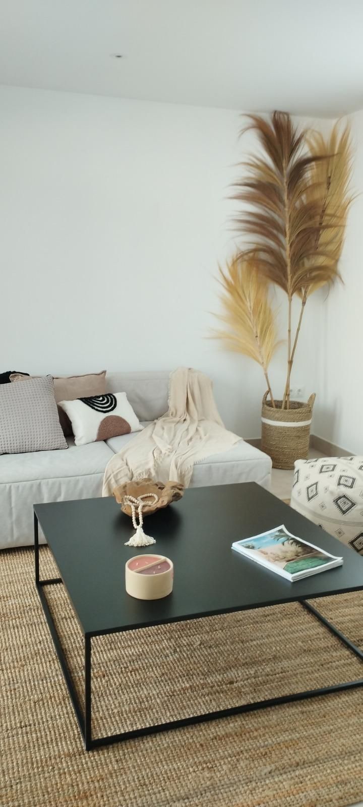 Sala de estar minimalista con mesa de centro negra, alfombra tejida, sofá blanco y decoración de hierba de la Pampa alta.