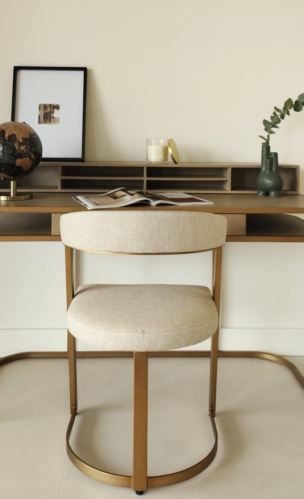 Escritorio moderno con silla color crema, escritorio de madera, cuadro y jarrón pequeño en una habitación minimalista.