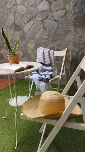 Muebles de patio con sillas blancas, un sombrero de paja, una toalla a rayas y una planta en maceta