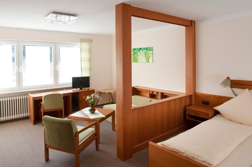 Hotelzimmer mit Einzelbett, Schreibtisch, Sitzecke und Raumteiler aus Holz.