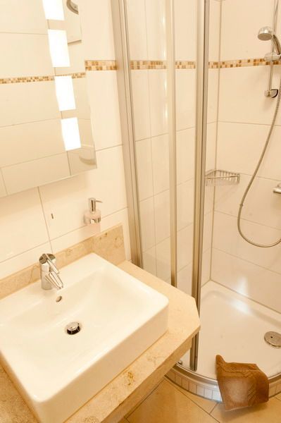 Badezimmer mit weißem Waschbecken, Dusche und beigen Fliesen.