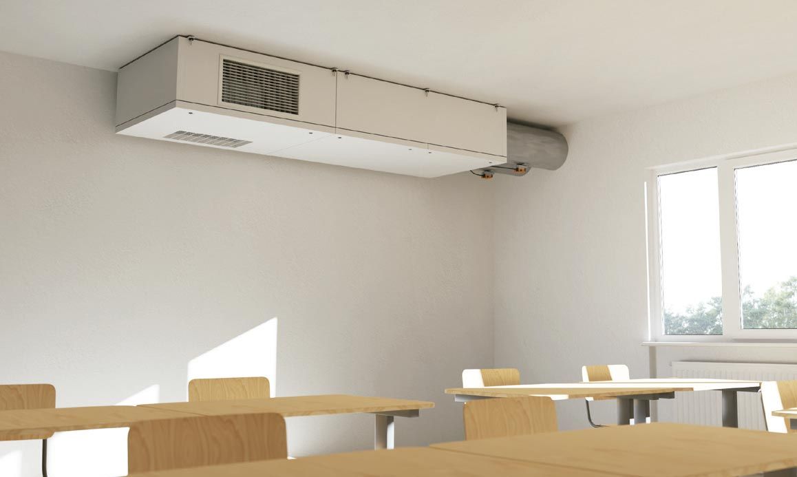 Aula luminosa con pupitres de madera, aire acondicionado de pared y luz natural que entra por una ventana.