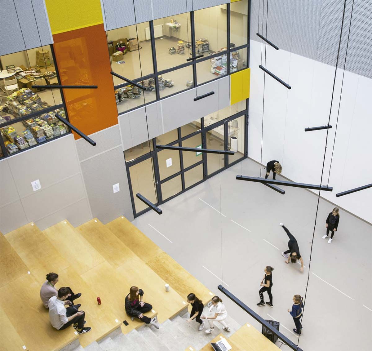 Gimnasio cubierto con escaladores en cuerdas y una gran pared, visible desde las gradas superiores.