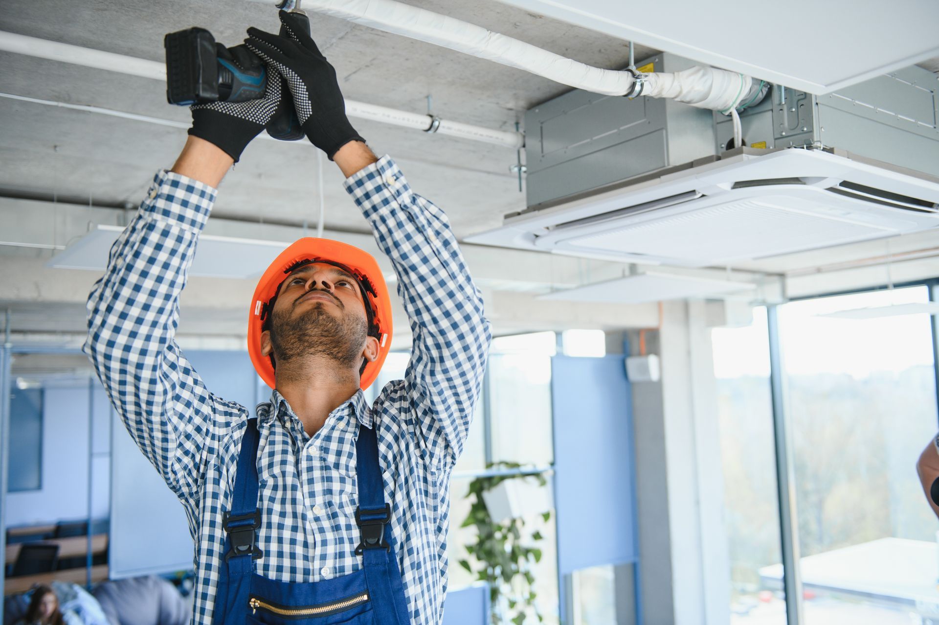 Hombre con mono y casco instalando cableado eléctrico en un techo.