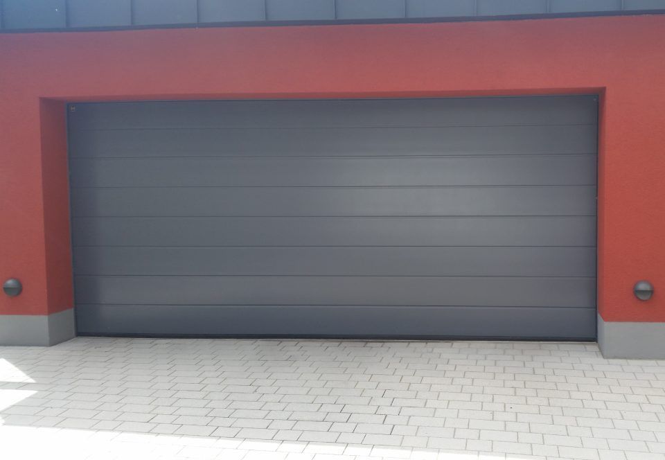 Beier André Die Holzwürmer Graues Garagentor neben roter Wand