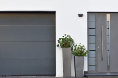 Graues Garagentor neben einer grauen Haustür mit Glaseinsatz