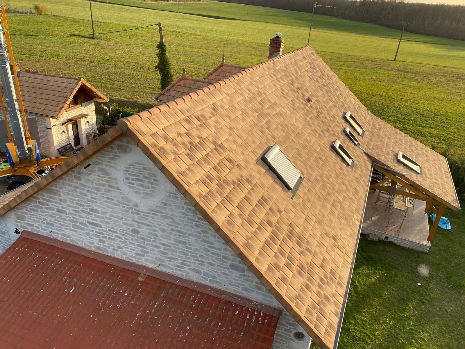 Vue aérienne d'une maison au toit de tuiles beiges et au revêtement en pierre. Autour, une pelouse verdoyante.