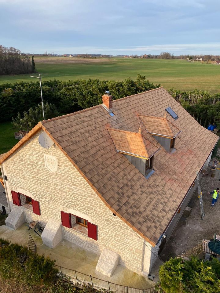 Maison en pierre avec volets rouges et toit brun sur fond de champ vert.