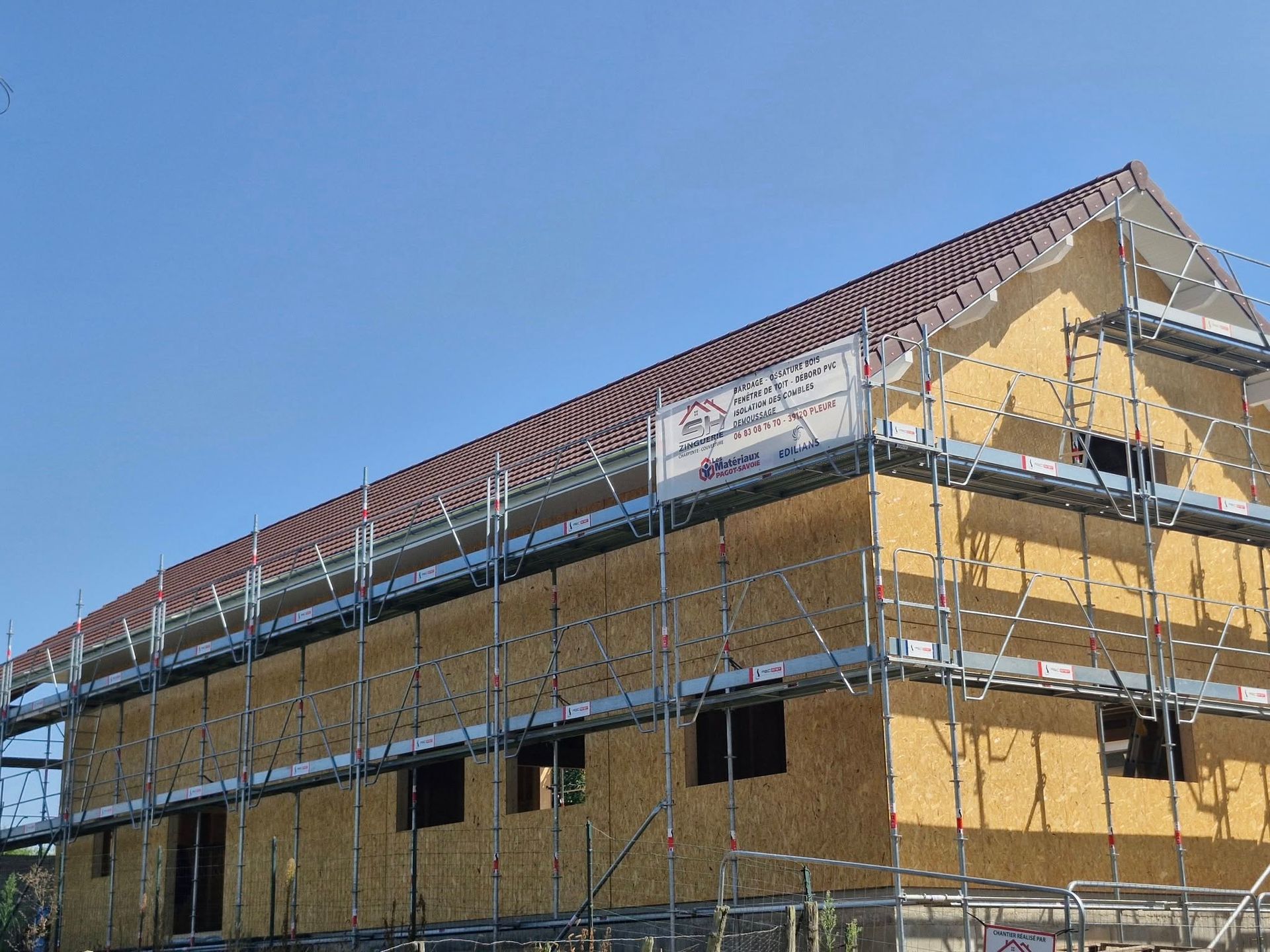 Bâtiment en construction avec échafaudage, revêtement jaune, toit marron et un ciel bleu clair.