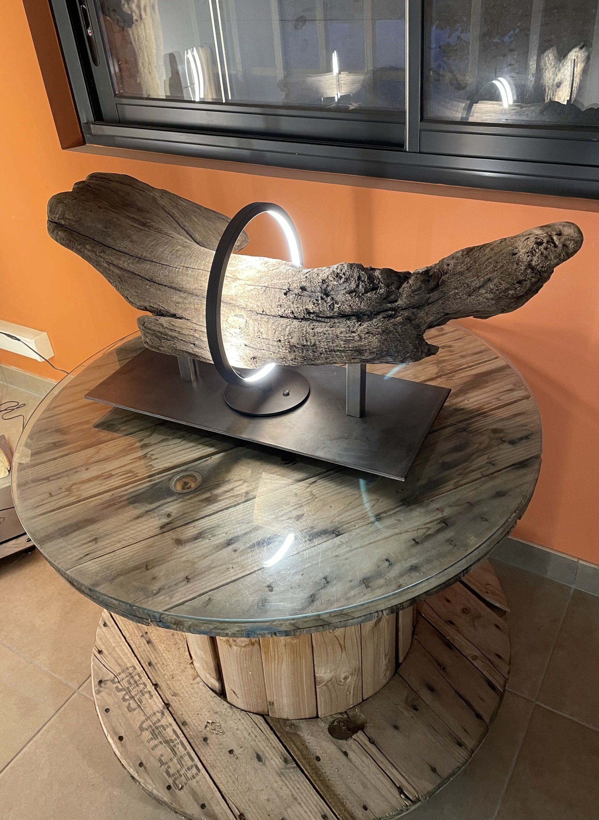 Un luminaire blanc circulaire entourant du bois flotté sur socle.