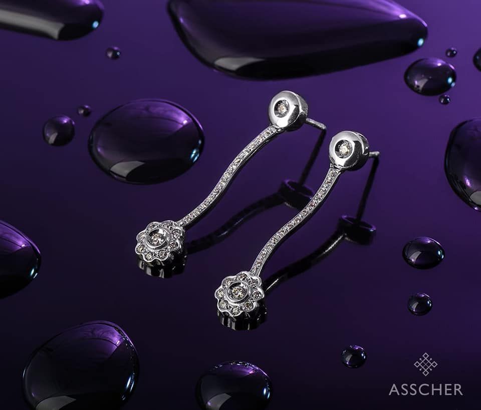 Un par de pendientes Asscher se encuentran sobre una superficie morada.