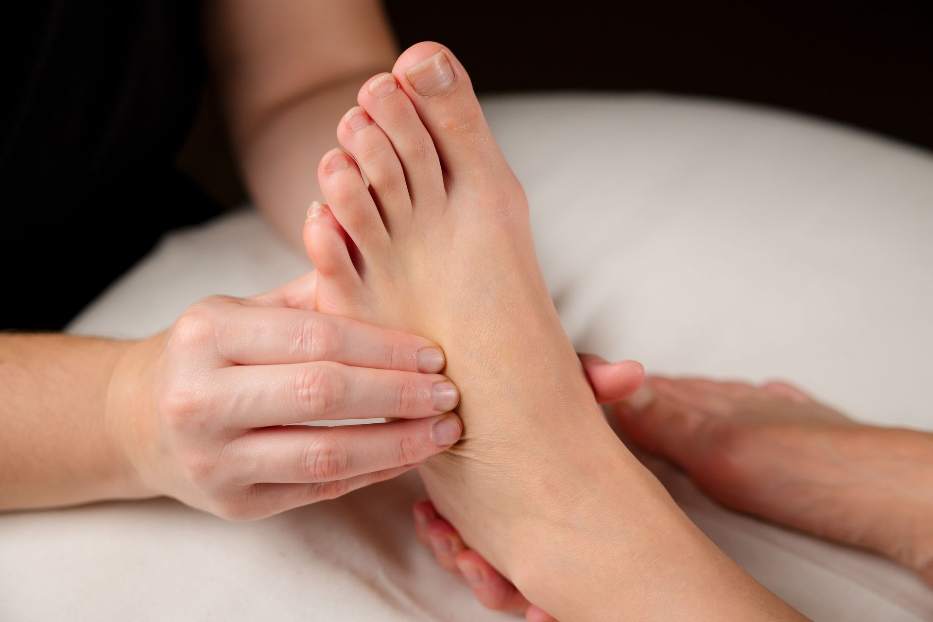 Une personne recevant un massage des pieds, les mains appuyant doucement sur la plante de son pied.