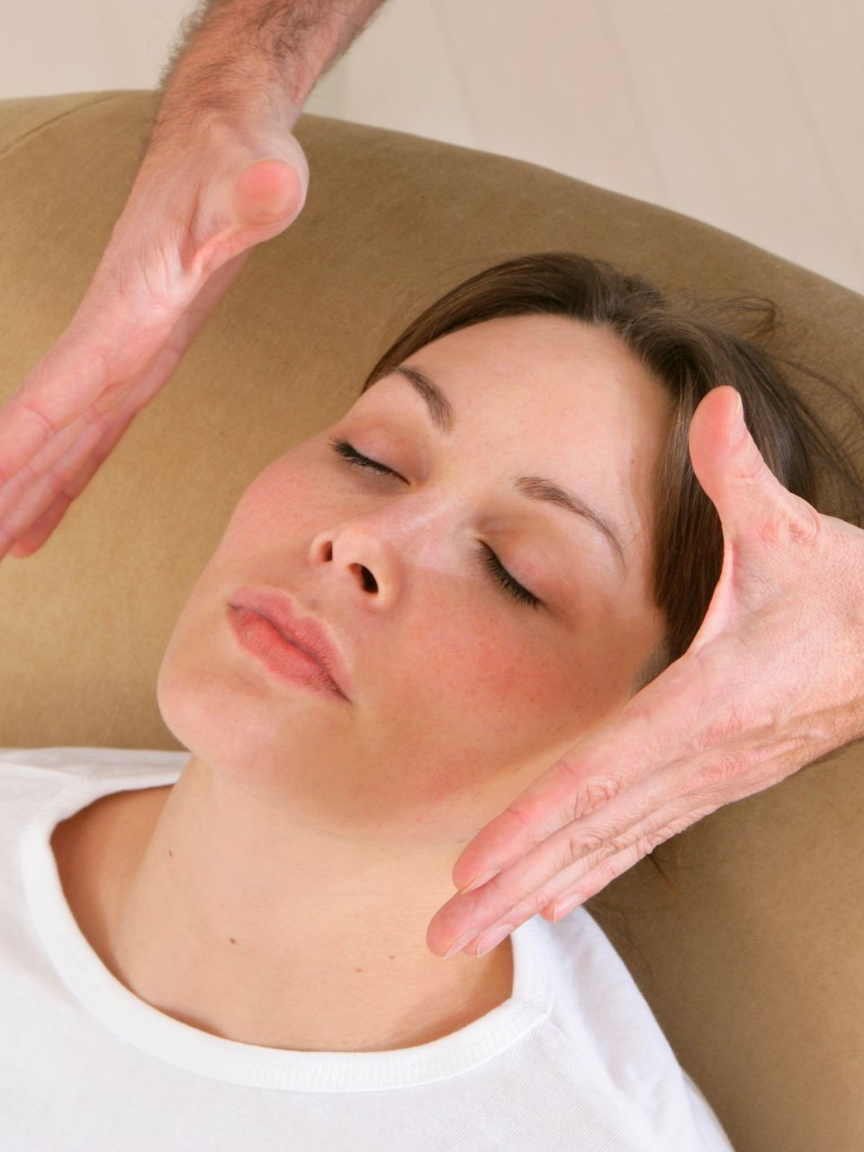 Une personne allongée, les yeux fermés, se faisant masser doucement le visage.