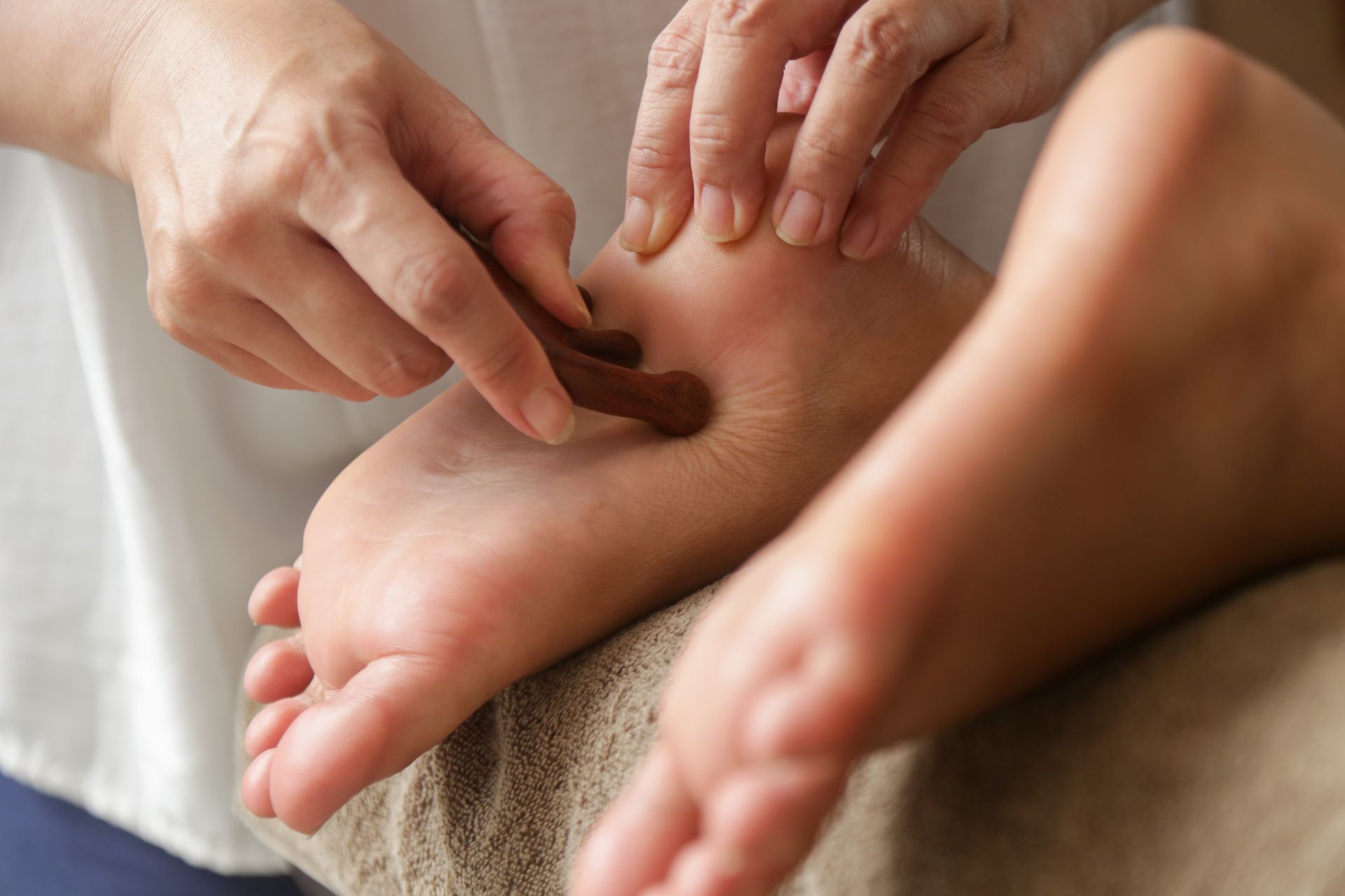 Lors d'une séance de réflexologie, une personne utilise un outil de massage en bois pour appliquer une pression sur le talon du pied.