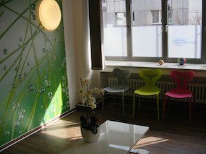 Wartezimmer mit grüner Fototapete und bunten Sitzen vor einem breiten Fenster