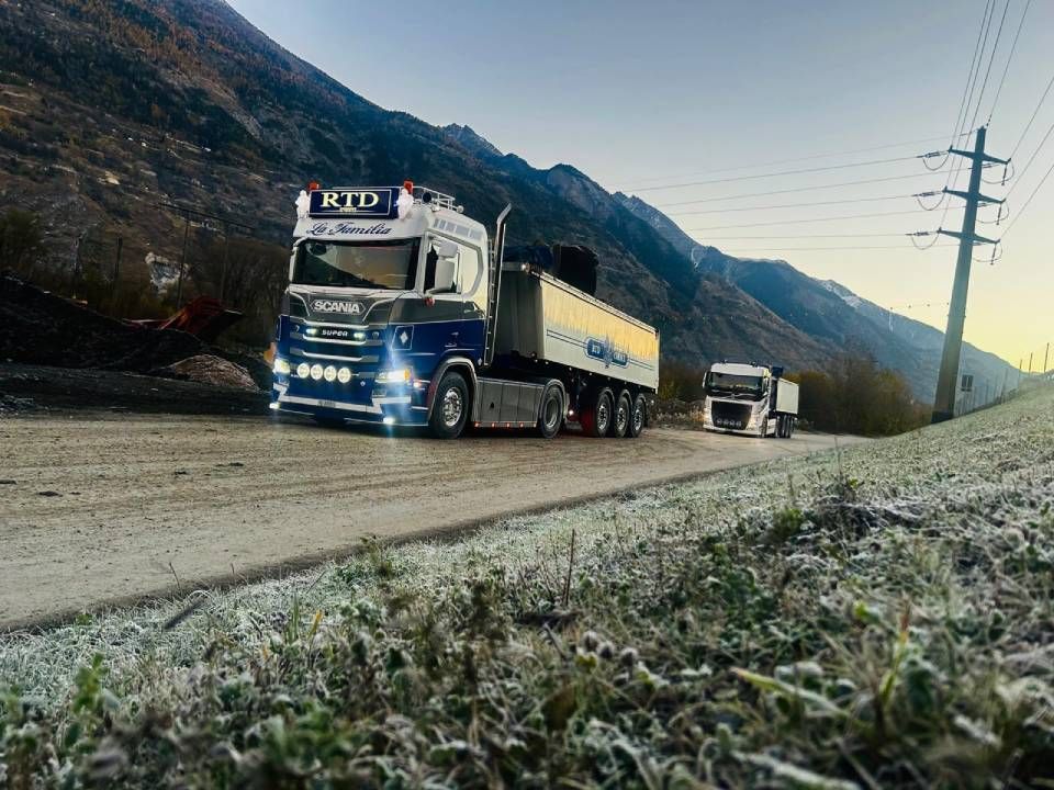 Un camion roule sur un chemin de terre à côté d'une montagne.