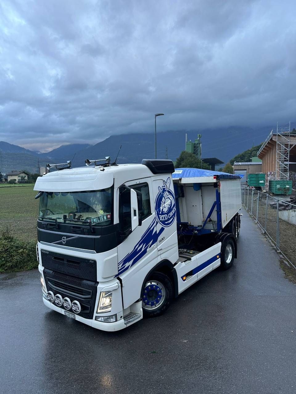 Un camion blanc et bleu roule sur une route mouillée.