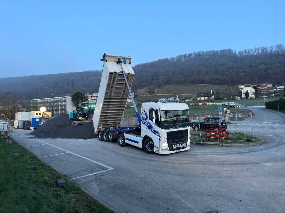 Un camion-benne blanc et bleu roule sur une route.