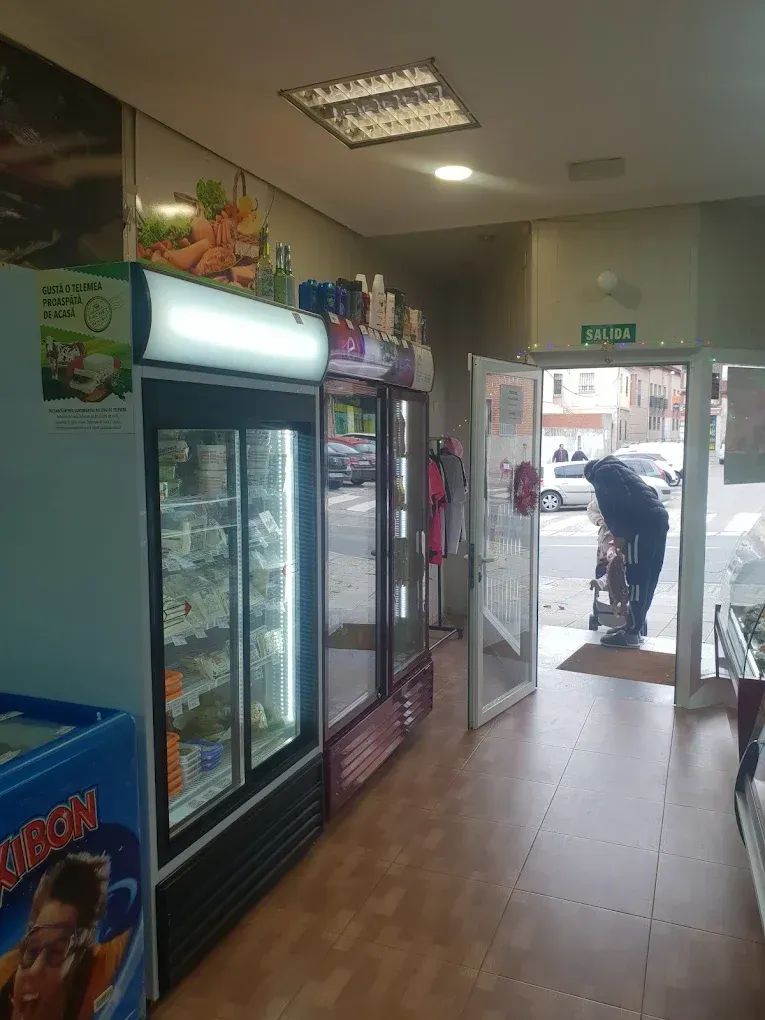 Dentro de una tienda: vitrinas refrigeradas, puerta abierta con persona afuera, iluminación fluorescente.