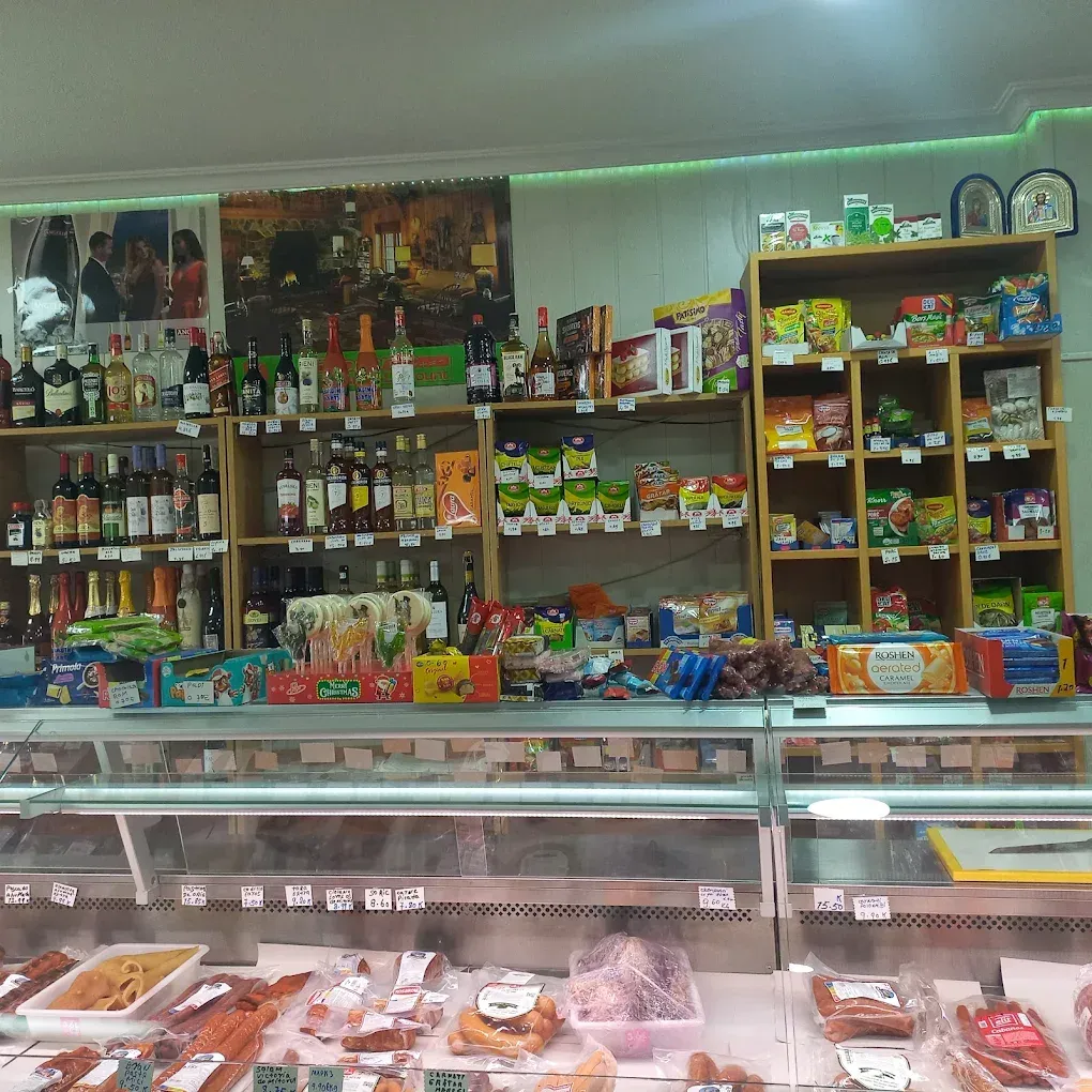 Interior de una tienda, con estantes de comida y bebidas detrás de una vitrina con diversas carnes.