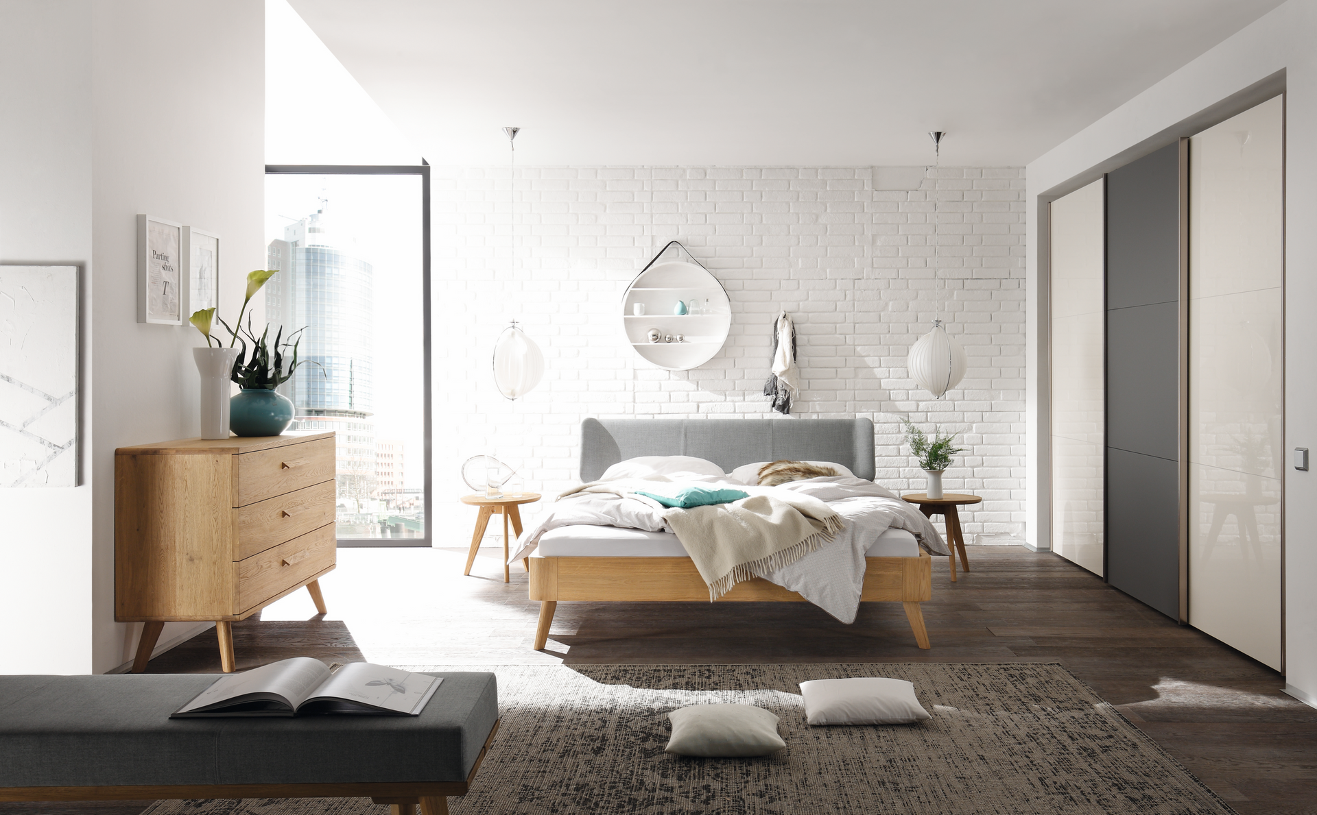 Modernes Schlafzimmer mit Holzmöbeln, Backsteinwand, großem Fenster, Teppich und dekorativen Akzenten.