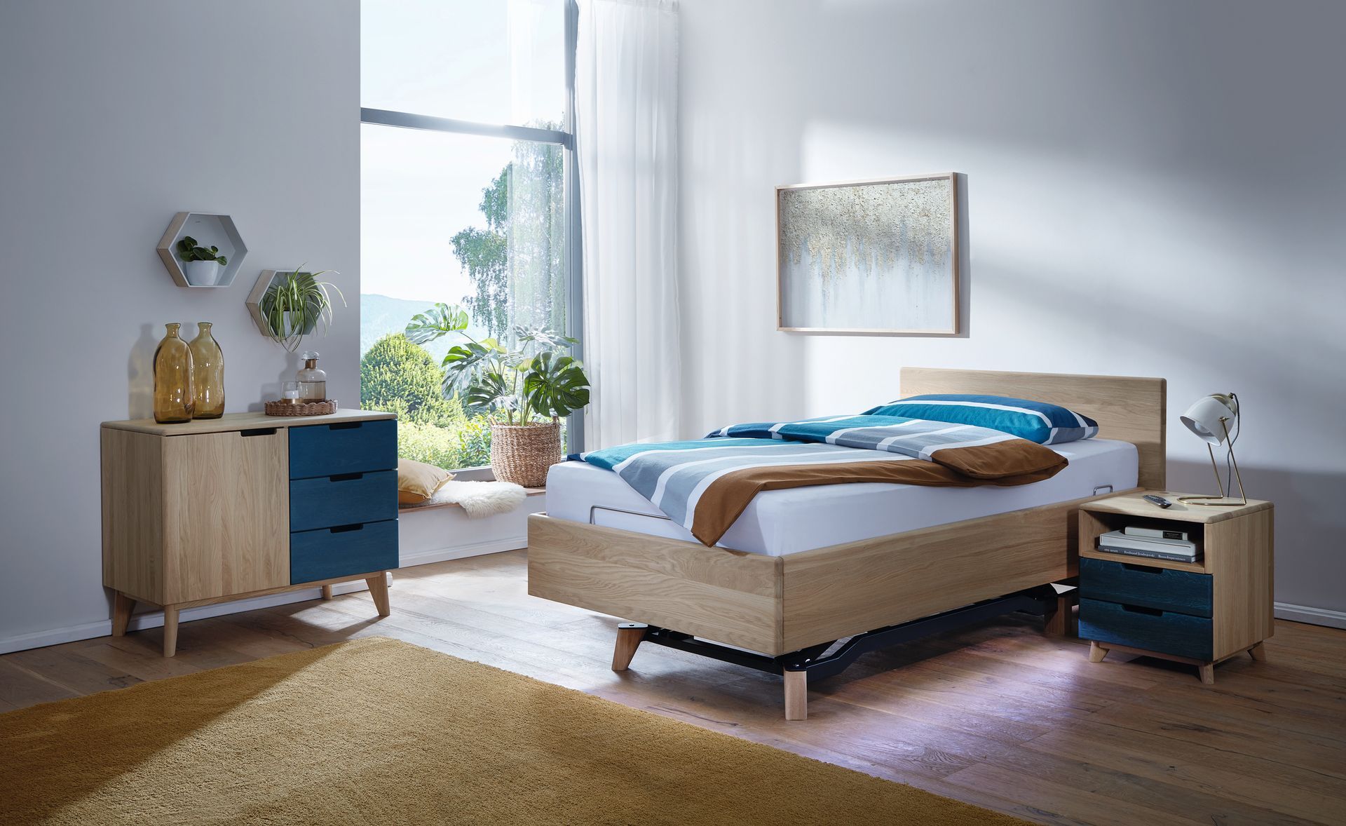 Schlafzimmer mit Holzmöbeln, blauen Akzenten, großem Fenster, Teppich und Kunstwerken.
