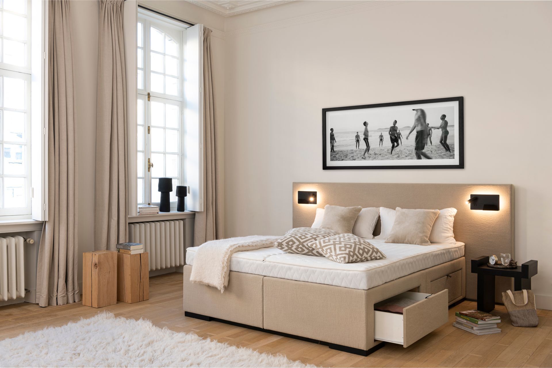 Schlafzimmer mit beigefarbenem Bett, offener Kommode, Fenster, neutralen Vorhängen, Kunstwerken und Nachttisch. Schlafzimmer mit beigefarbenem Bett, offener Kommode, Fenster, neutralen Vorhängen, Kunstwerken und Nachttisch.