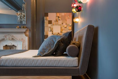 Schlafzimmerinterieur mit Bett, Kissen und dekorativer Beleuchtung an einer blauen Wand.