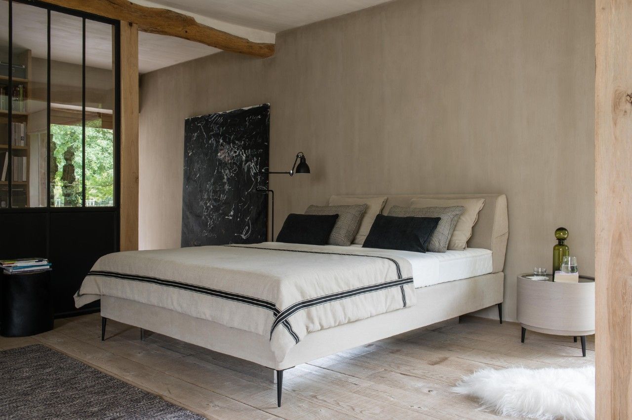 Schlafzimmer mit Bett, Nachttisch und großer schwarzer Wandverkleidung vor beiger Wand; Holzboden und Glastür. Schlafzimmer mit Bett, Nachttisch und großer schwarzer Wandverkleidung vor beiger Wand; Holzboden und Glastür.