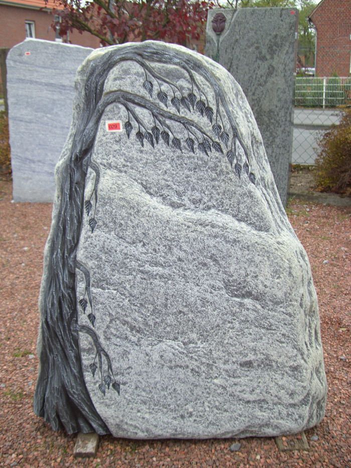Auf einem Friedhof liegt ein großer Felsen mit einem darin eingemeißelten Baum.