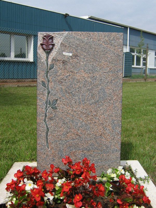 Ein Grabstein mit einer Rose darauf und Blumen vor einem Gebäude