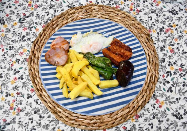 Un plato de comida con patatas fritas, jamón, huevos y pimientos sobre un mantel individual.