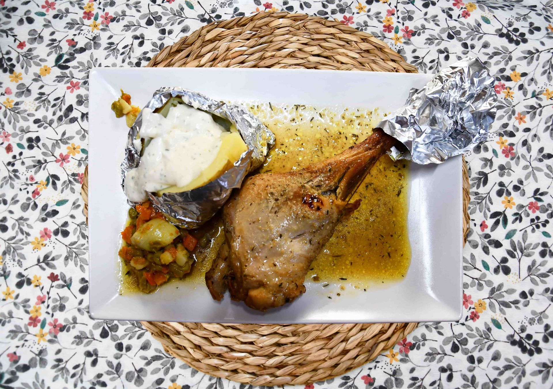 Un plato blanco cubierto con carne, patatas y verduras sobre una mesa.