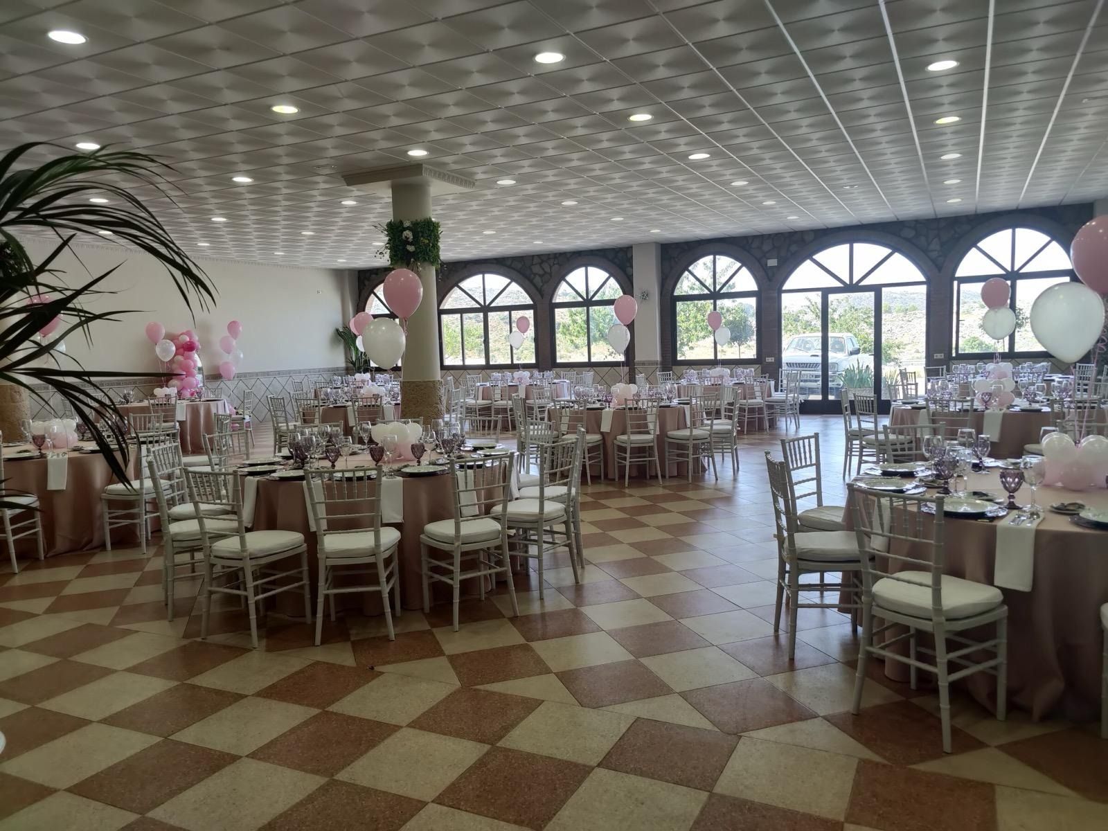 Una gran sala con mesas y sillas y globos en el techo.