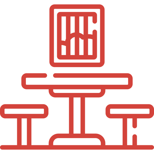 Un icono rojo de una mesa y sillas sobre un fondo blanco.
