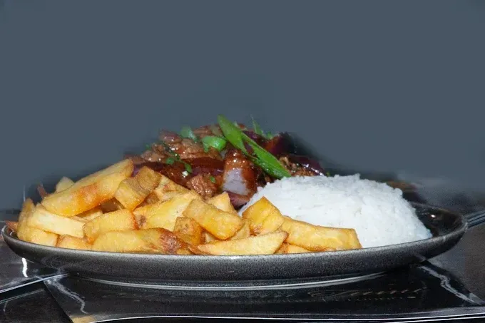 Plato de comida con patatas fritas, arroz y carne glaseada.