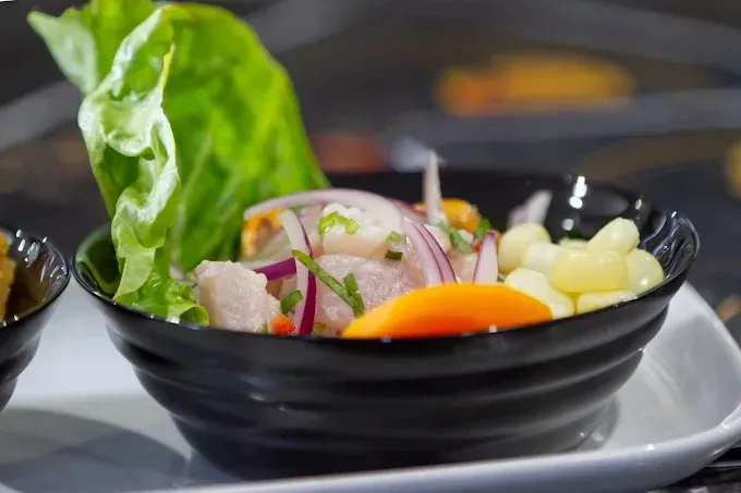 Ceviche en un tazón negro con cebolla roja, maíz y lechuga en un plato blanco.