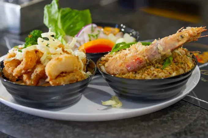 Plato de mariscos fritos con salsa para mojar. Incluye camarones tempura sobre arroz, vieiras fritas y ceviche.