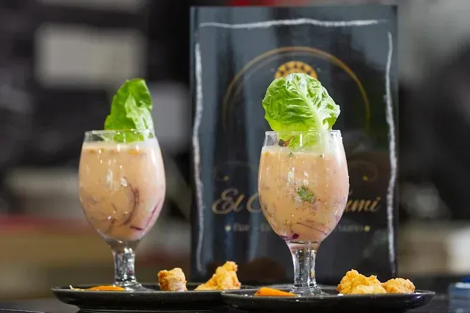 Dos cócteles con guarnición de lechuga delante de un tablero de menú oscuro, pequeños trozos de pan en primer plano.