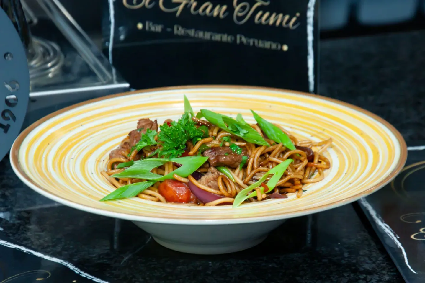 Bowl de Lomo Saltado Peruano: fideos, carne, cebolla, tomate, cebolla verde, ambiente de restaurante.