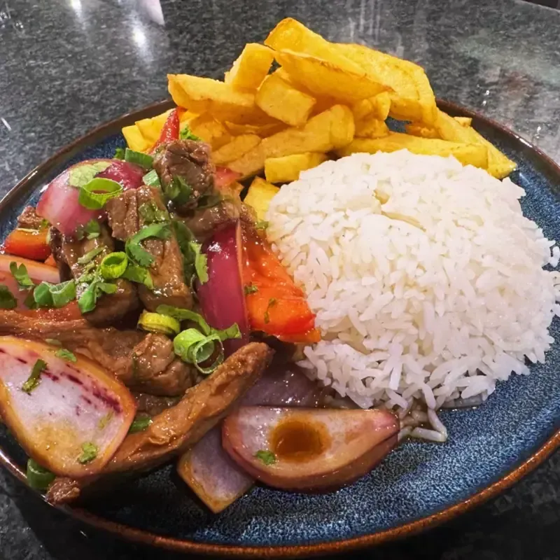 Plato peruano de Lomo Saltado: carne de res salteada con cebollas, tomates, arroz y papas fritas.