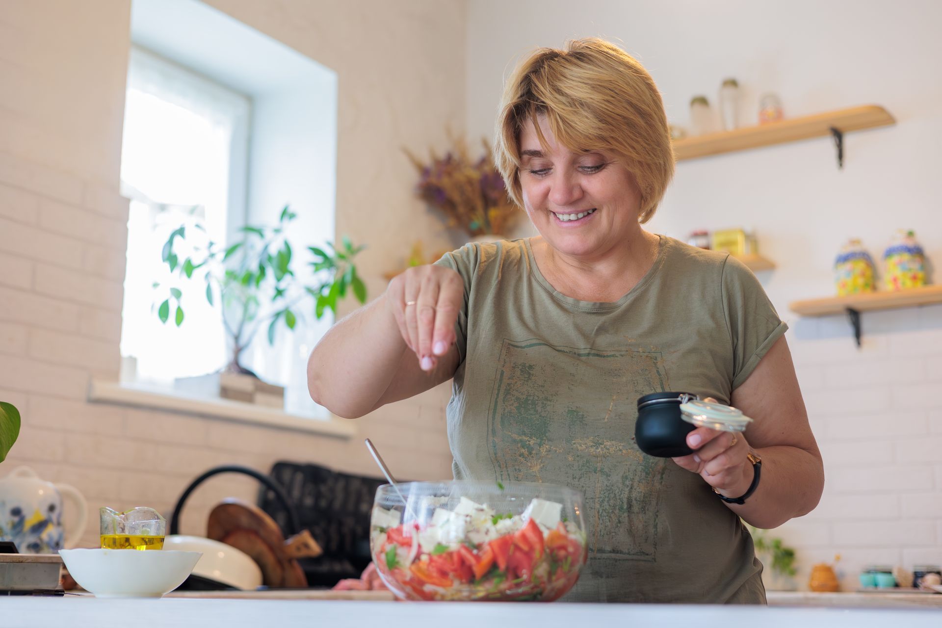 Une femme saupoudre d'épices une salade dans un saladier dans sa cuisine.